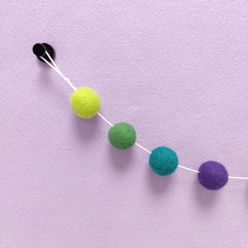 Zoom sur les pompons vert citron, vert feuille, violet ultra et vert canard avec la boucle de fixation de la guirlande 