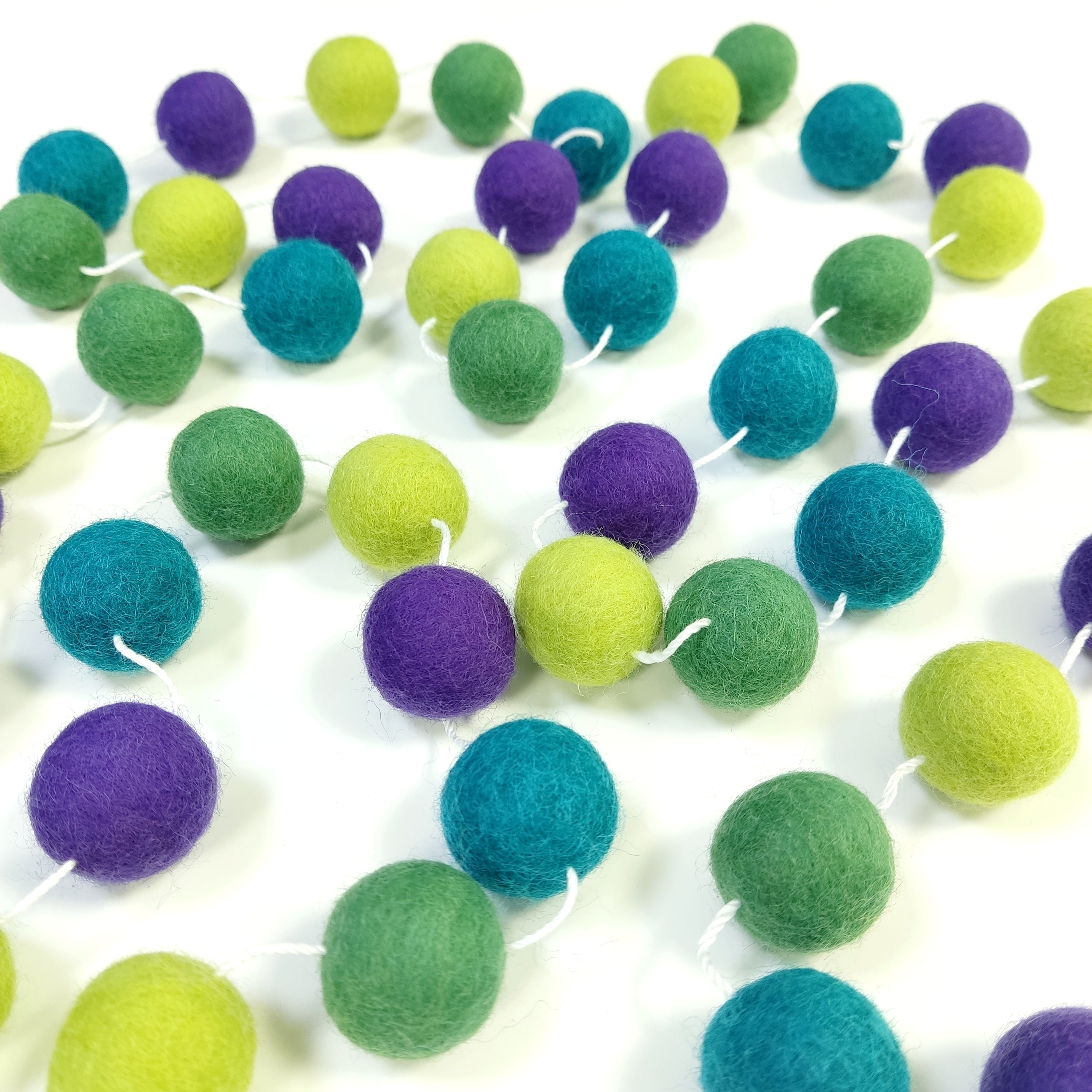 Guirlande en boules de feutre vert violet étalée sur une table avec les pompons espacés