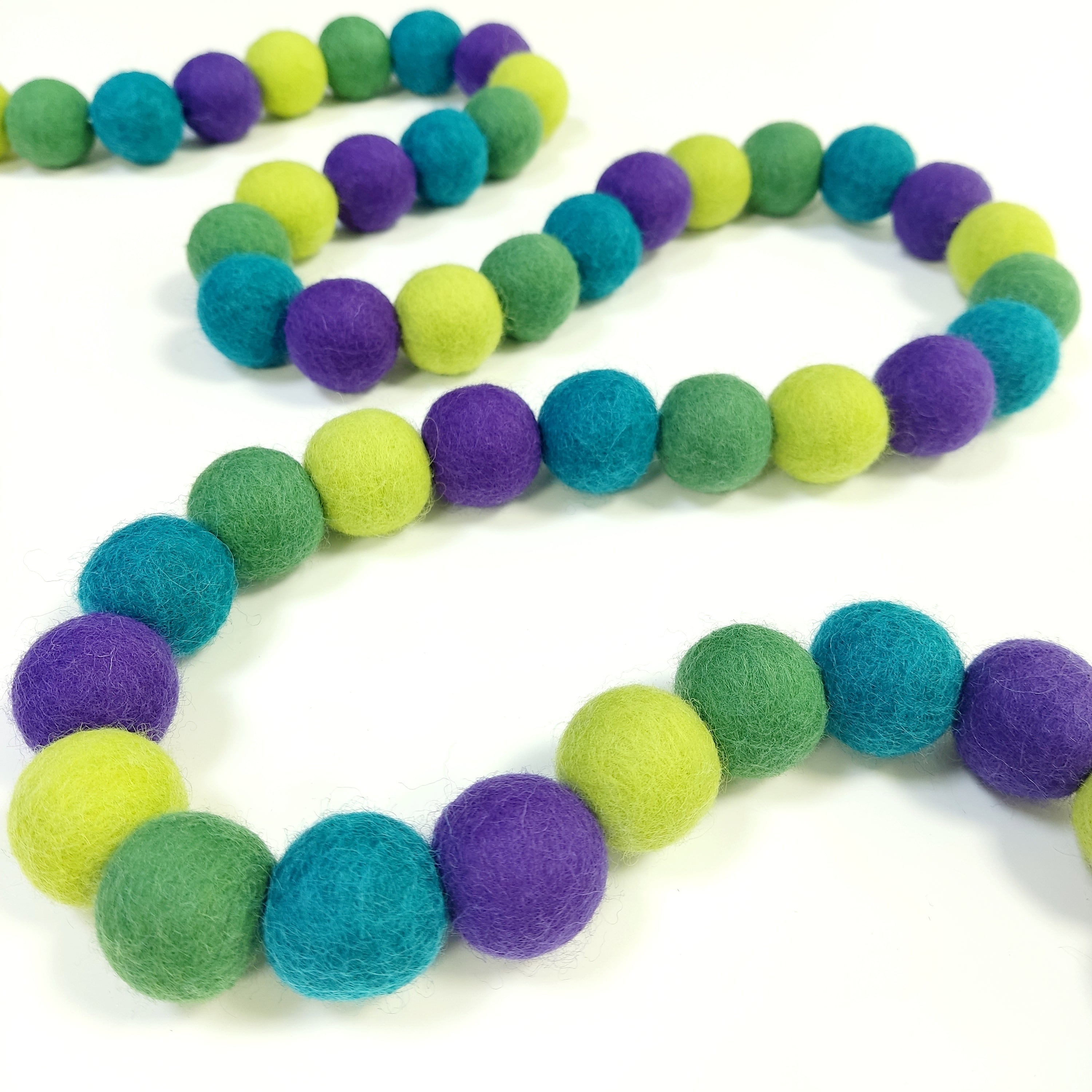 Guirlandes de pompons vert violet posée en serpentin sur une table avec les pompons rassemblés sur le fil