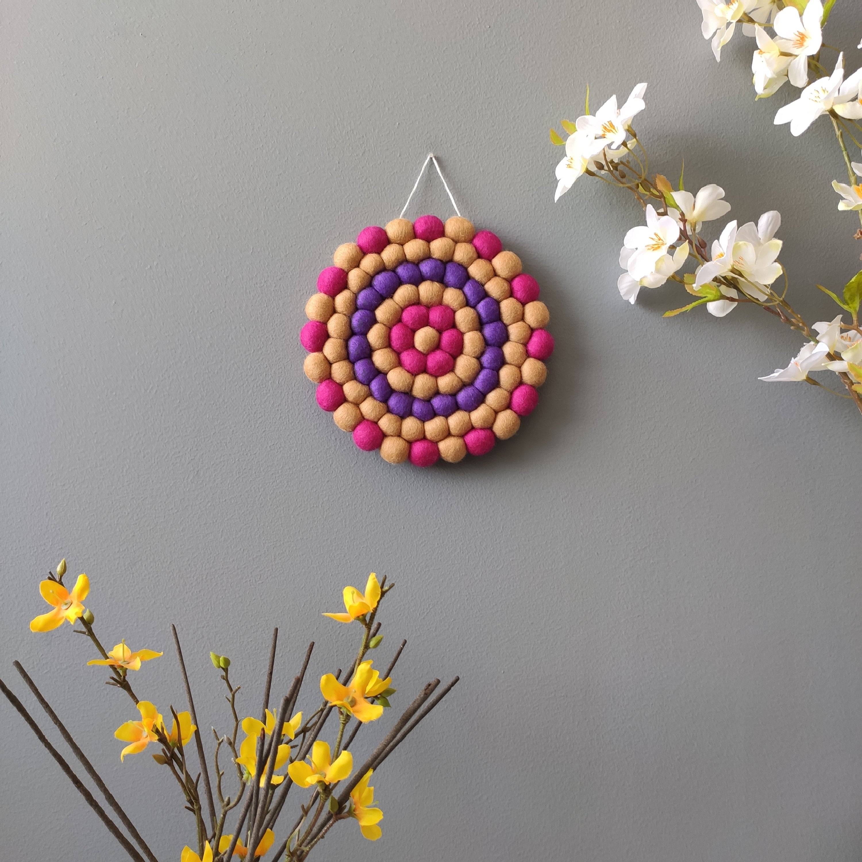 Tapisserie ronde Electra en pompons Mérinos – Décoration murale bohème aux teintes beige, violet et fuchsia – CELAINEDECO