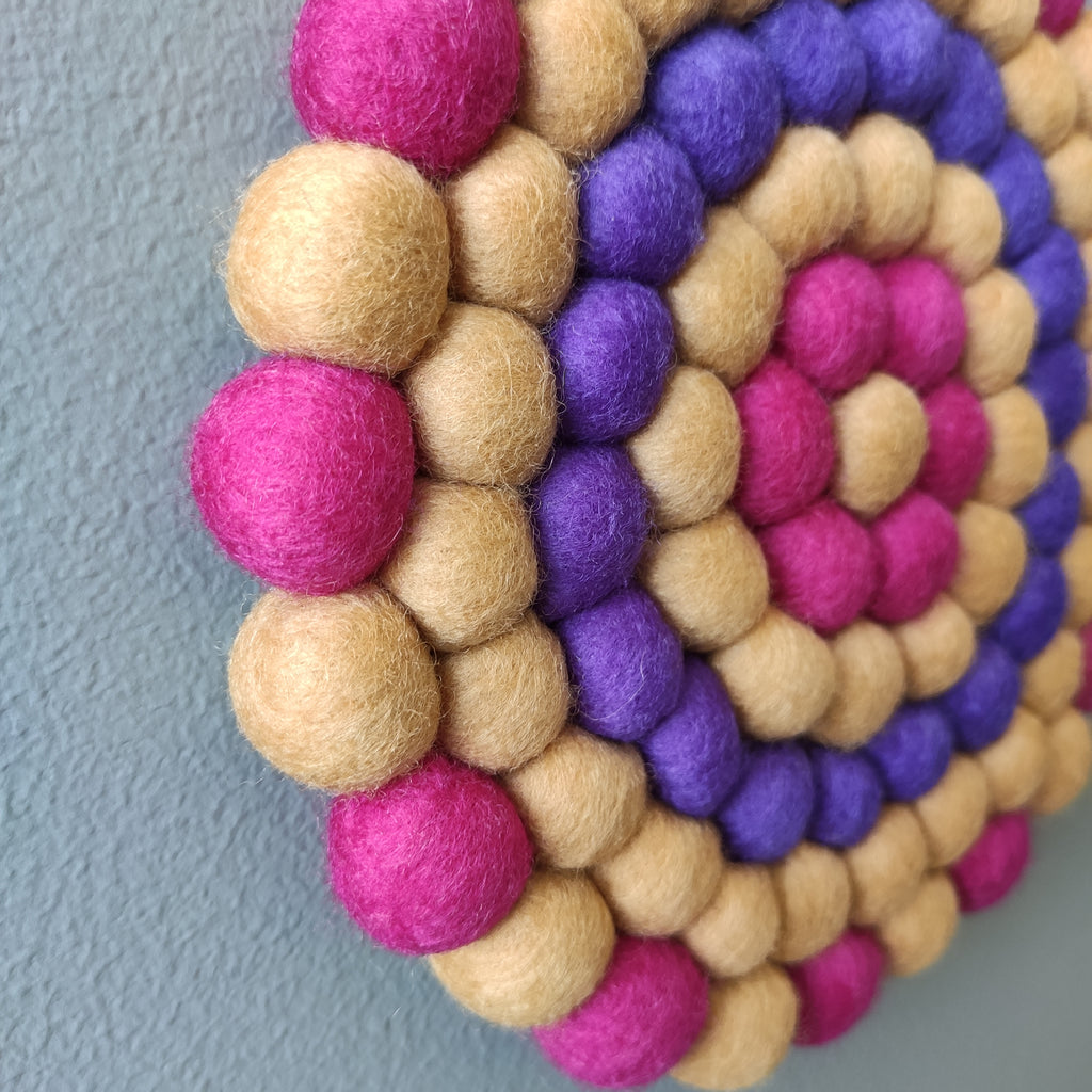 Zoom sur les pompons en laine Mérinos de la tapisserie Electra – Détail texture beige sable, violet électrique et rose fuchsia