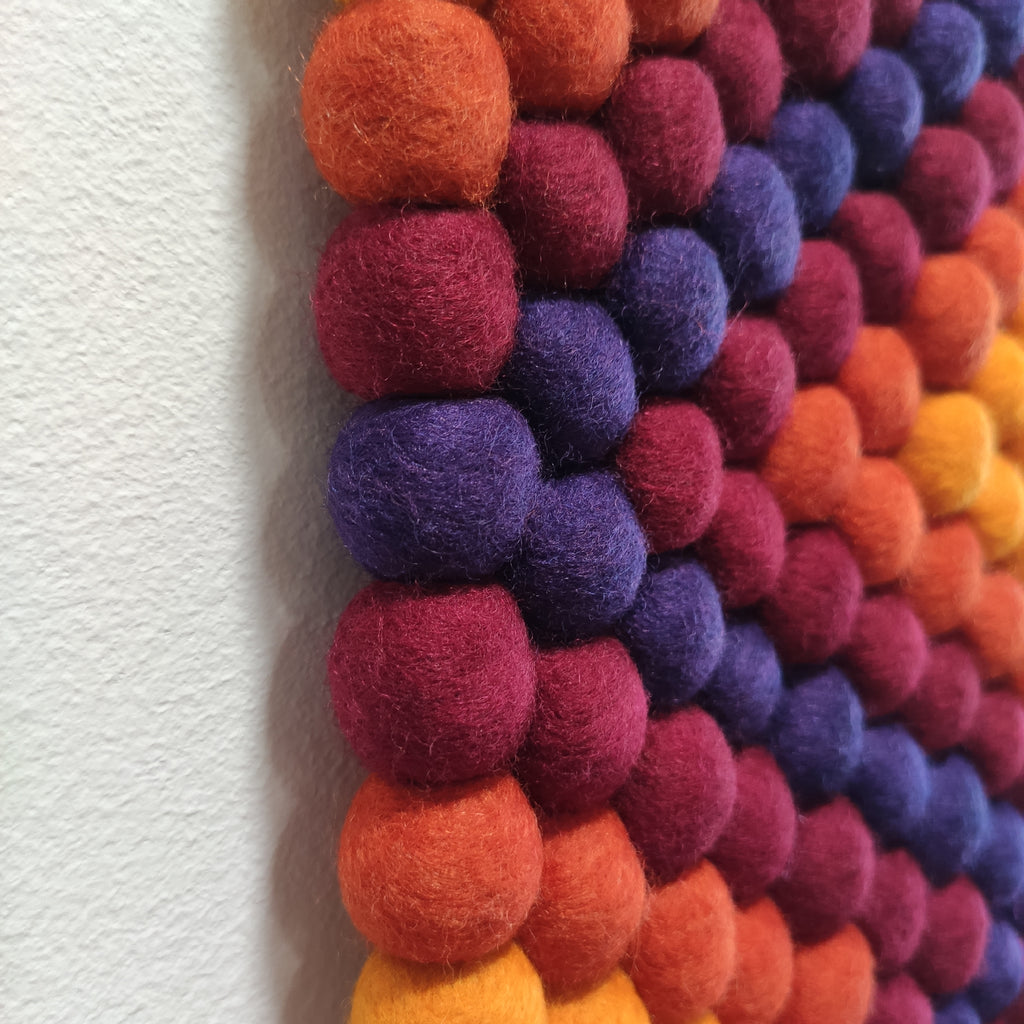 Détail des pompons de feutre en laine Mérinos de la tapisserie murale Ipanema – couleurs orange, jaune, bordeaux et violet