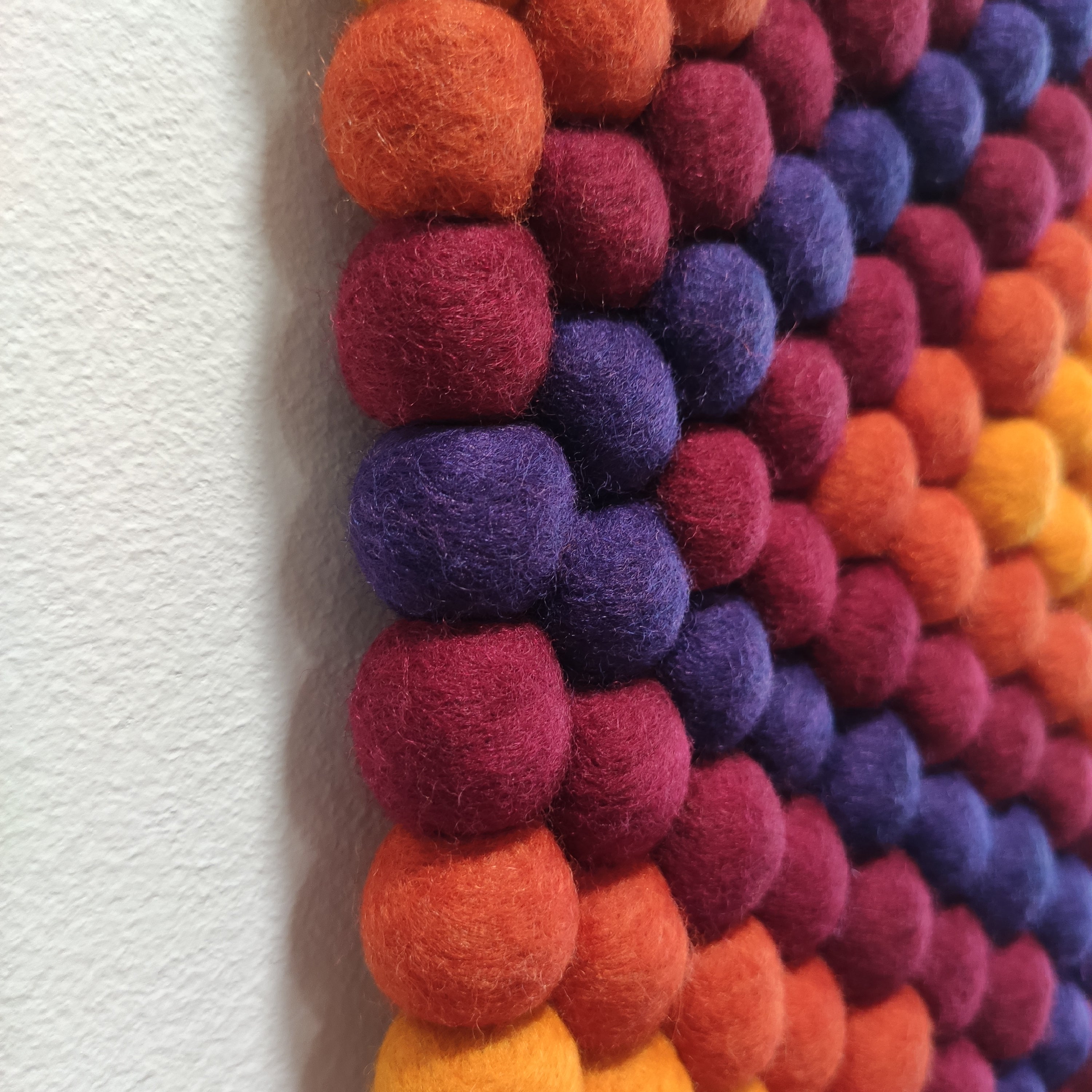 Détail des pompons de feutre en laine Mérinos de la tapisserie murale Ipanema – couleurs orange, jaune, bordeaux et violet