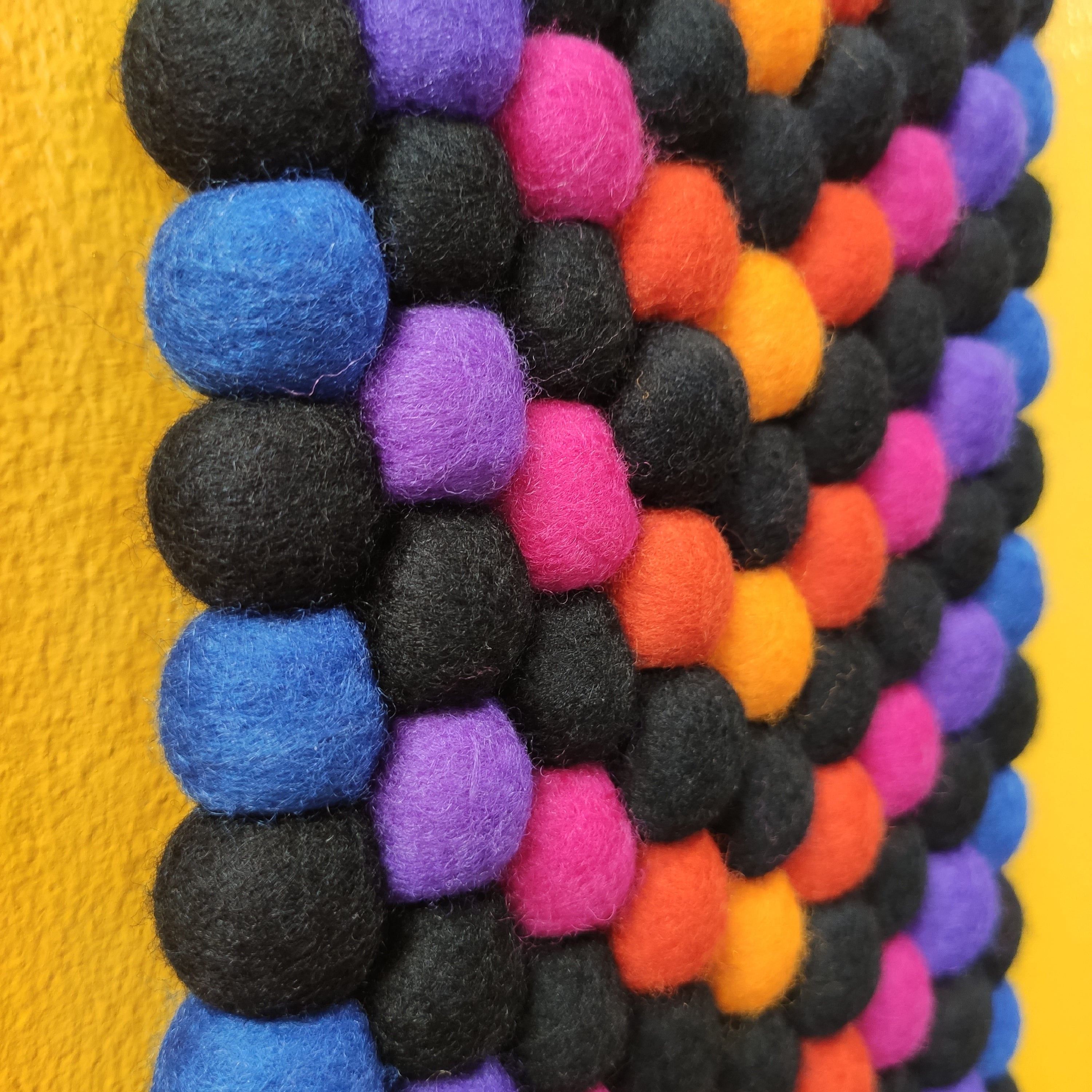 Détail pompons feutrés tapisserie Quetzal – dégradé bleu indigo, violet, fuchsia, orange, jaune tournesol