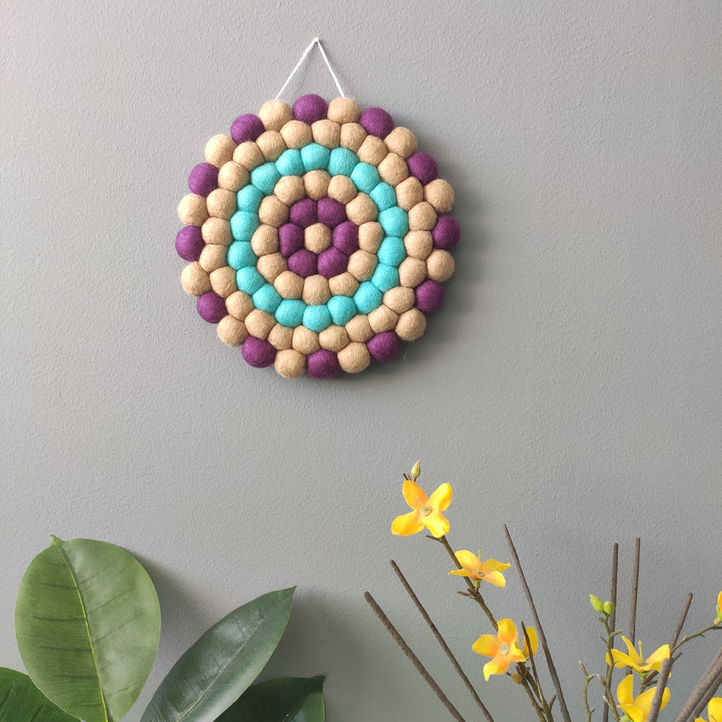 Mise en scene de la tapisserie Solstice sur mur gris avec fleurs – laine Mérinos tons beige, violine et turquoise – artisanat français – CELAINEDECO