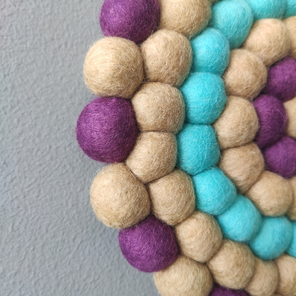 Détail des pompons feutrés de la tapisserie ronde Solstice – palette chromatique beige dune, violine profond, bleu lagon – CELAINEDECO