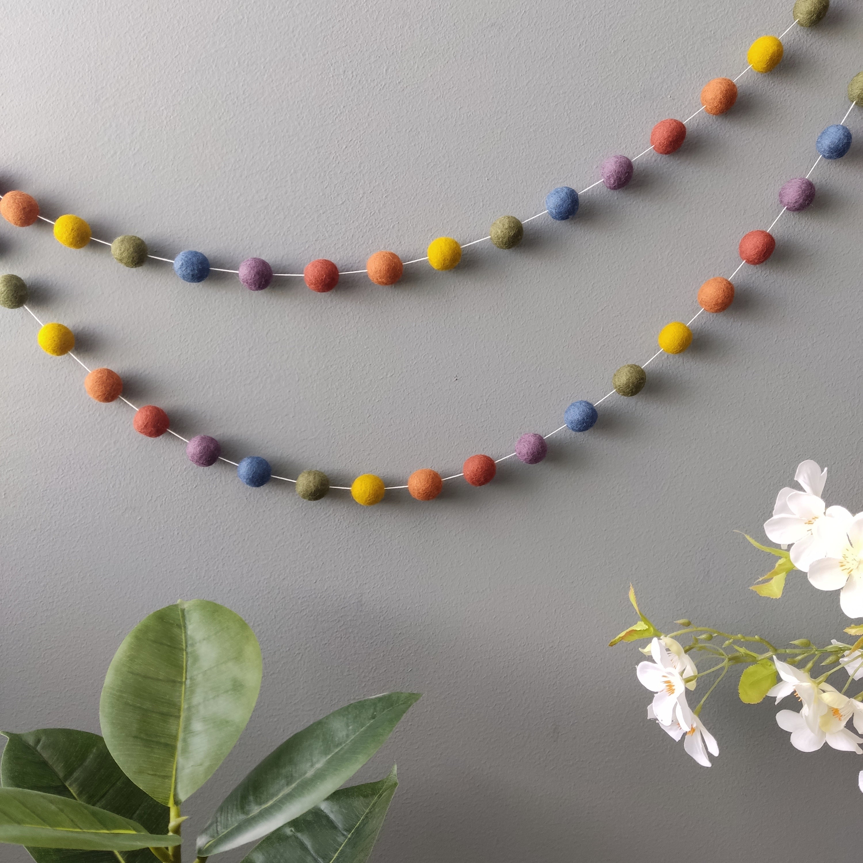 Handcrafted felt ball garland in vintage colors hanged on a grey wall